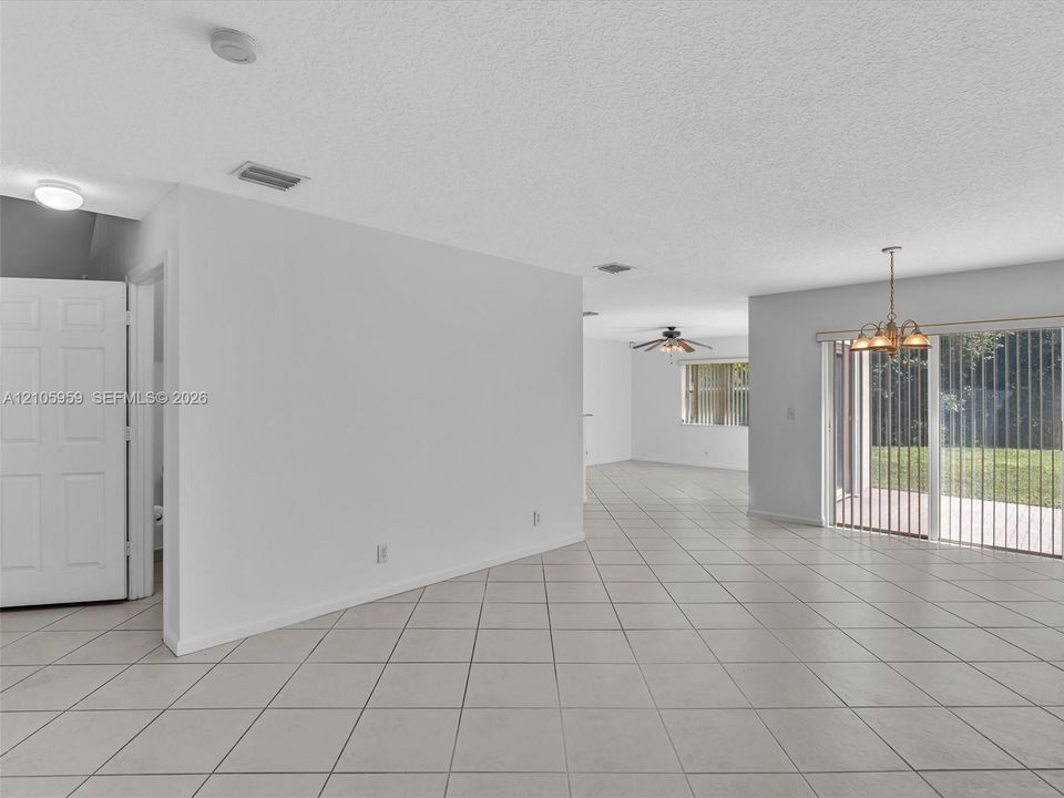 Open-concept interior featuring large-format neutral tile flooring, multi-pane sliding glass doors, a decorative multi-light chandelier, and recessed ceiling lighting