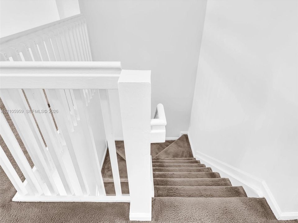 Staircase featuring a white balustrade with a square newel post and neutral carpeting