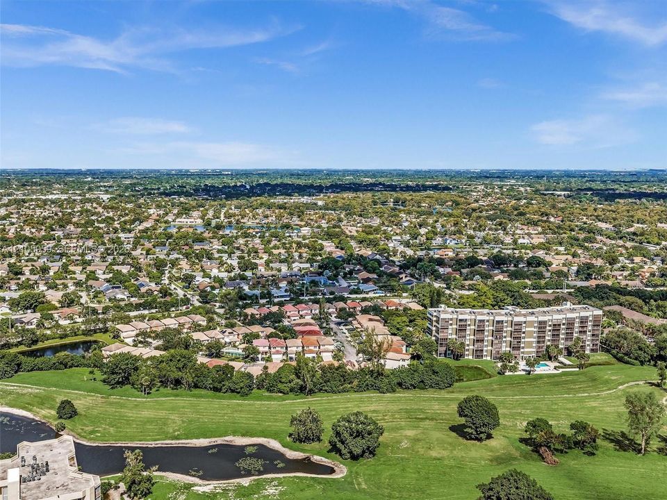 Aerial perspective of the residential area featuring a multi-story building, an expansive grass-covered expanse, and a natural pond