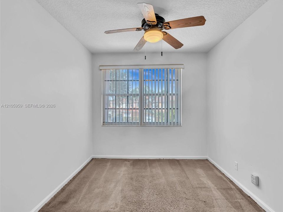 Neutral-toned wall interior featuring carpeting, a ceiling fan with integrated lighting, and a multi-pane window with vertical blinds