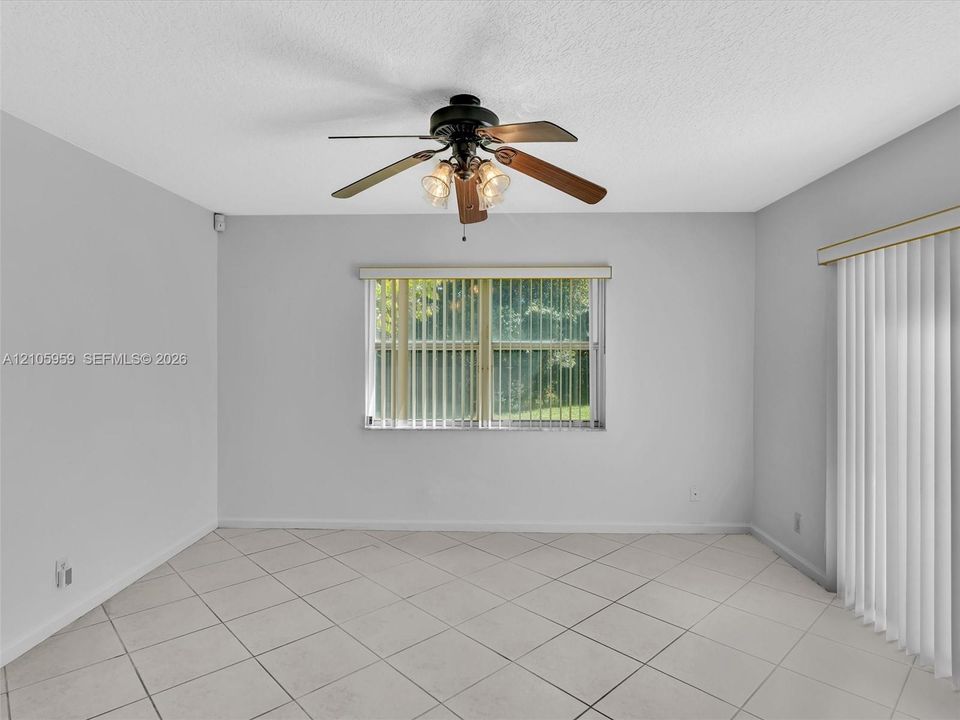 Neutral-toned tile flooring, ceiling fan with integrated light fixture, window with vertical blinds, and glass sliding door with vertical blinds