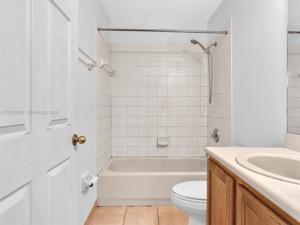 Bathroom featuring square-tile shower surround, handheld shower fixture, wood-finish cabinetry, integrated basin, and tiled flooring