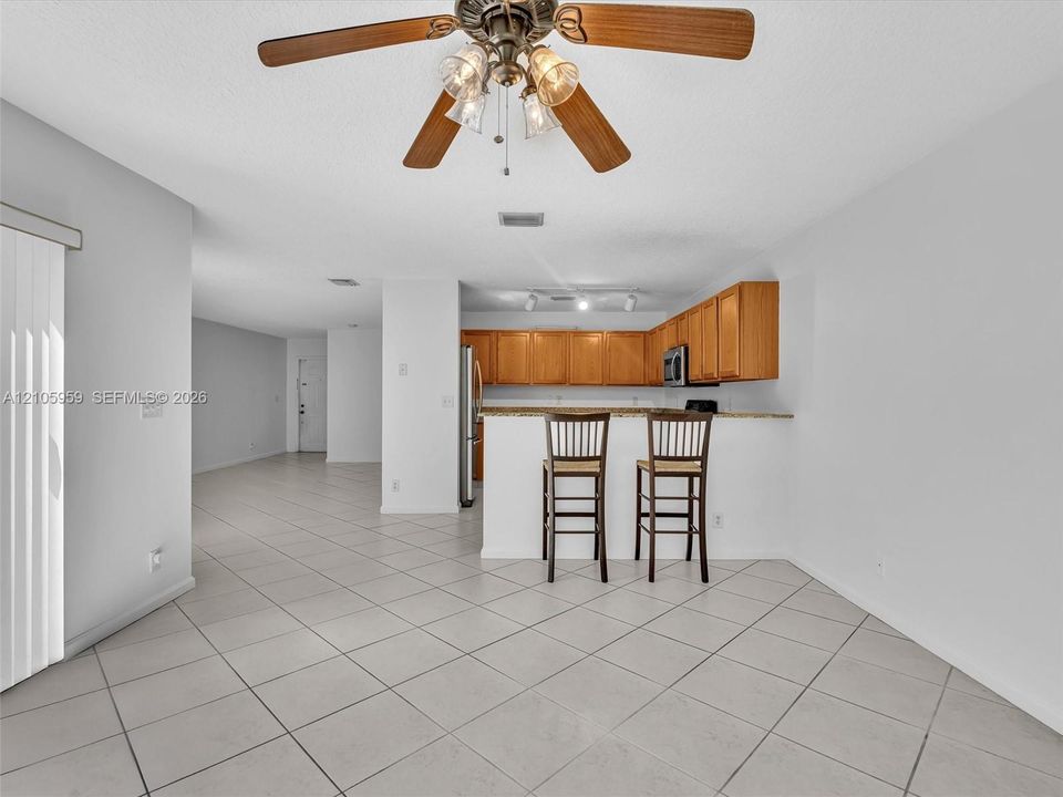 Ceramic tile flooring throughout, kitchen featuring wood cabinetry, stone-finish countertops, stainless steel appliances, and a ceiling fan with integrated lighting