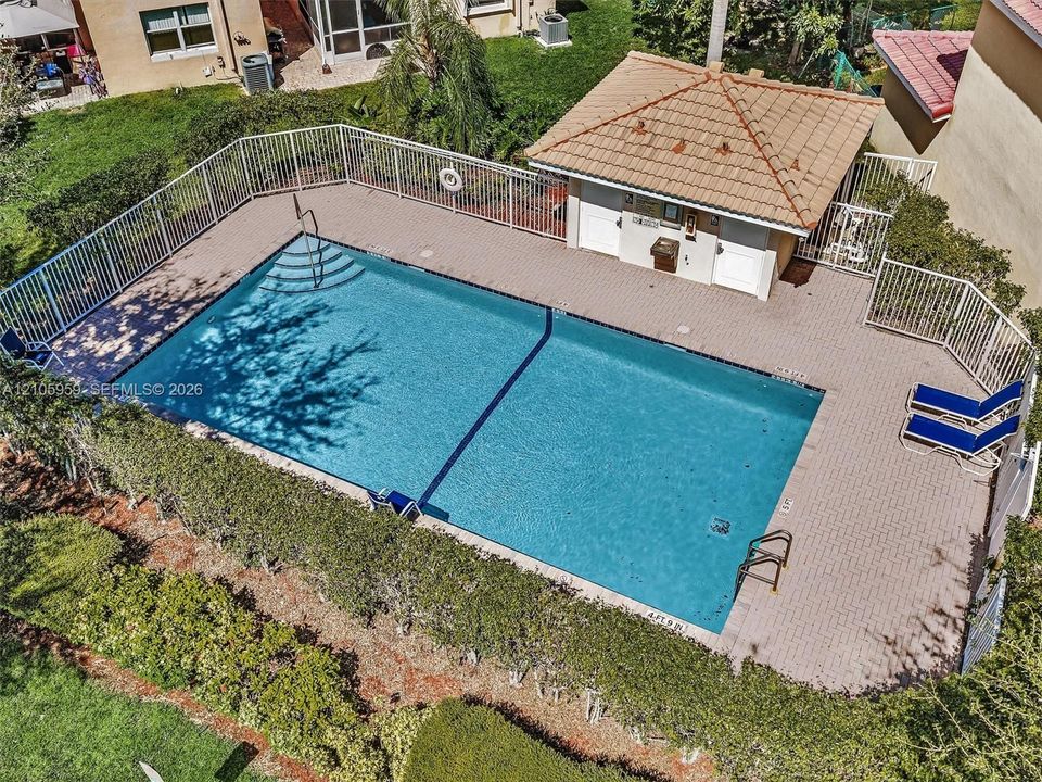 Swimming pool featuring a surrounding paver deck, built-in cabana, privacy fencing, and mature hedge landscaping
