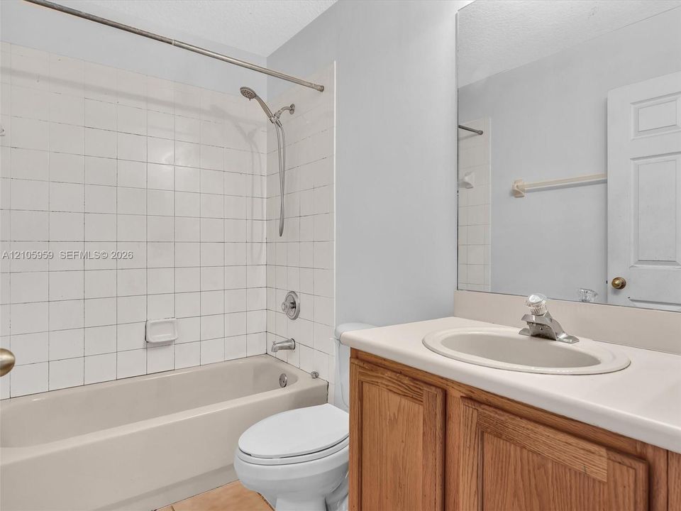 Bathroom featuring a white tile tub surround, handheld shower fixture, wood-finish vanity with an integrated countertop sink, and a full-width vanity mirror
