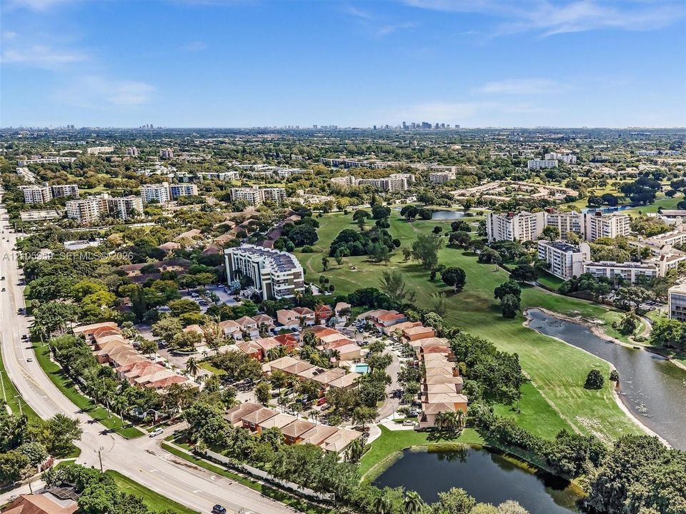 Aerial perspective featuring multi-unit residential buildings with tile roofing, surrounded by expansive landscaped grounds, mature trees, and waterfront features