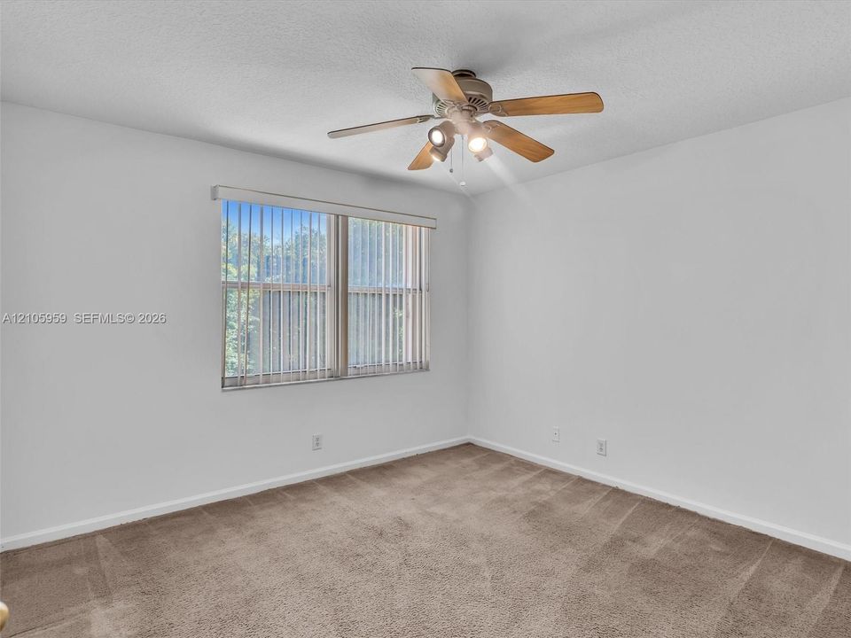 Neutral interior space featuring wall-to-wall carpeting, a multi-blade ceiling fan with integrated lighting, and vertical window blinds