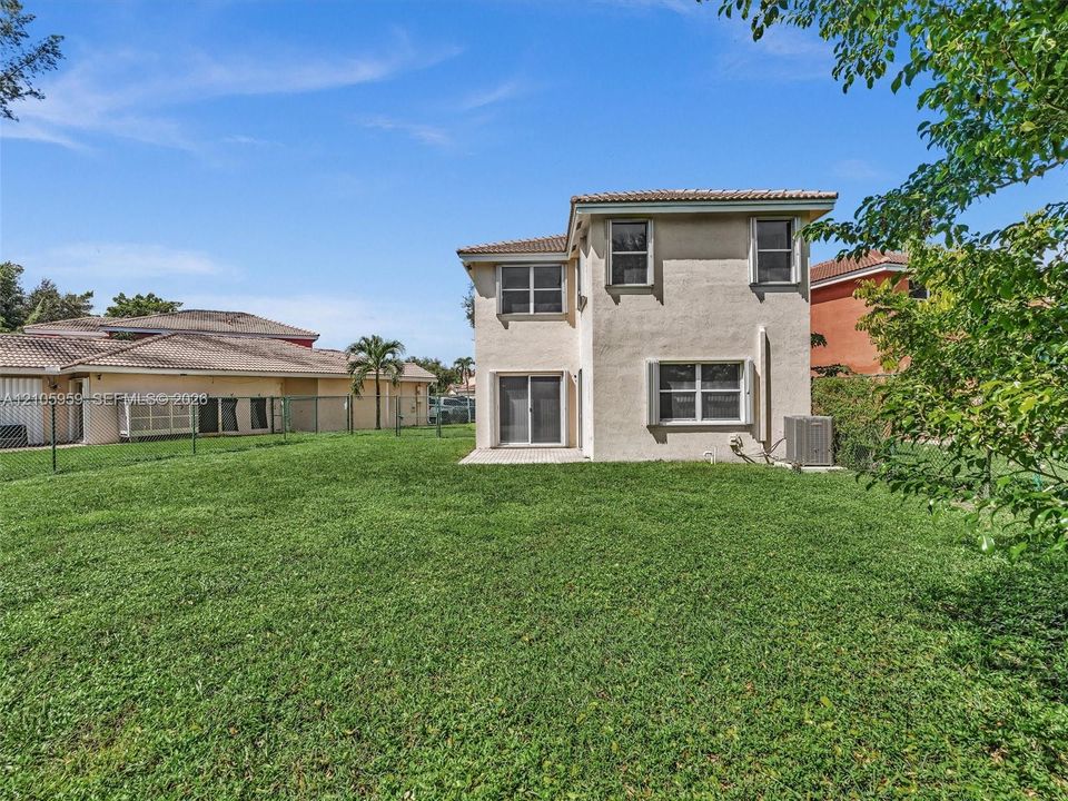 Two-story residence featuring a stucco exterior, concrete tile roofing, sliding glass door, and a fenced backyard with lawn space
