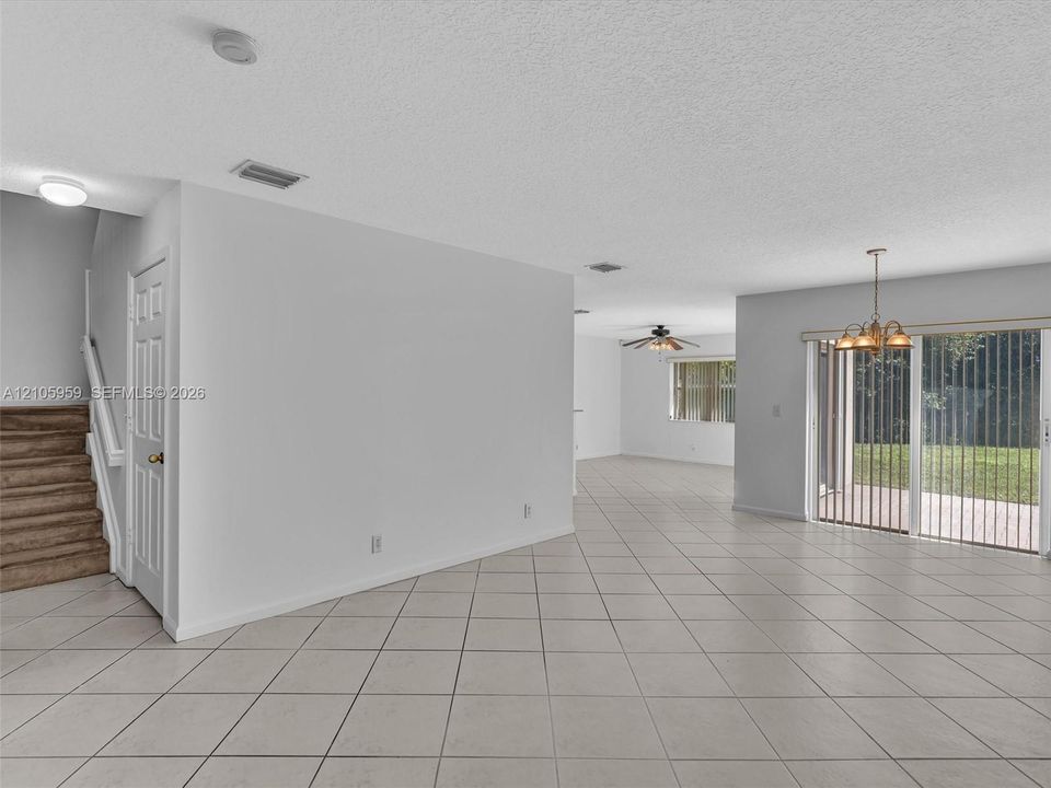 Interior space featuring large-format ceramic tile flooring, sliding glass patio doors, a classic chandelier, and a carpeted staircase