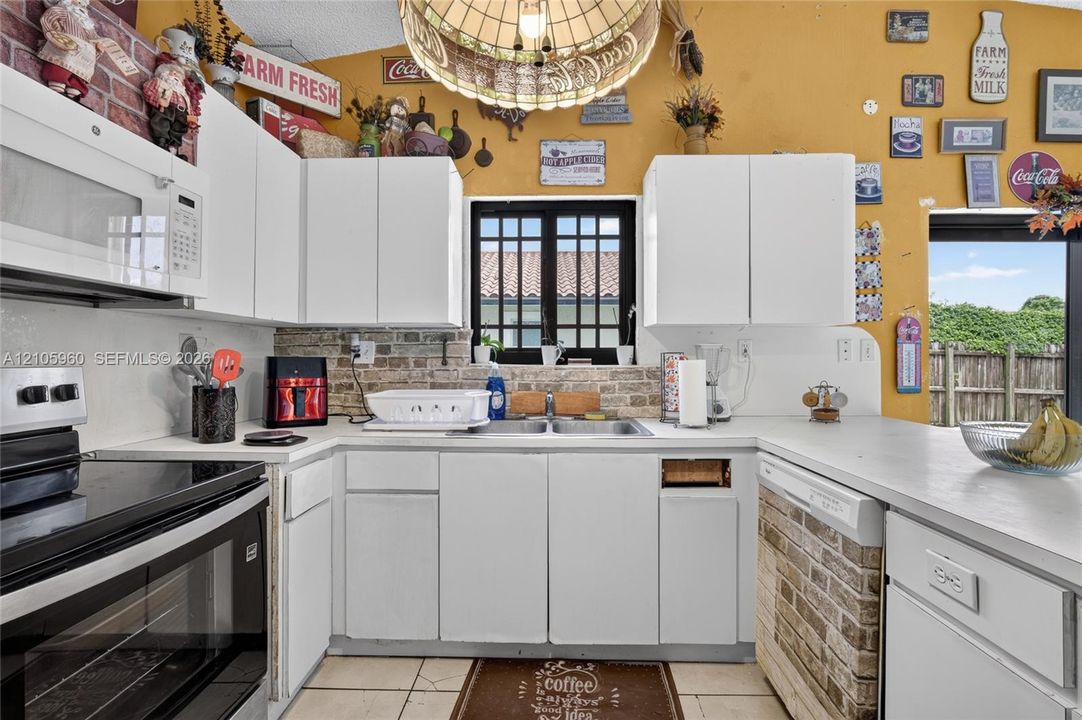 Kitchen featuring white cabinetry, brick backsplash detailing, double-basin sink, and a large pendant light fixture