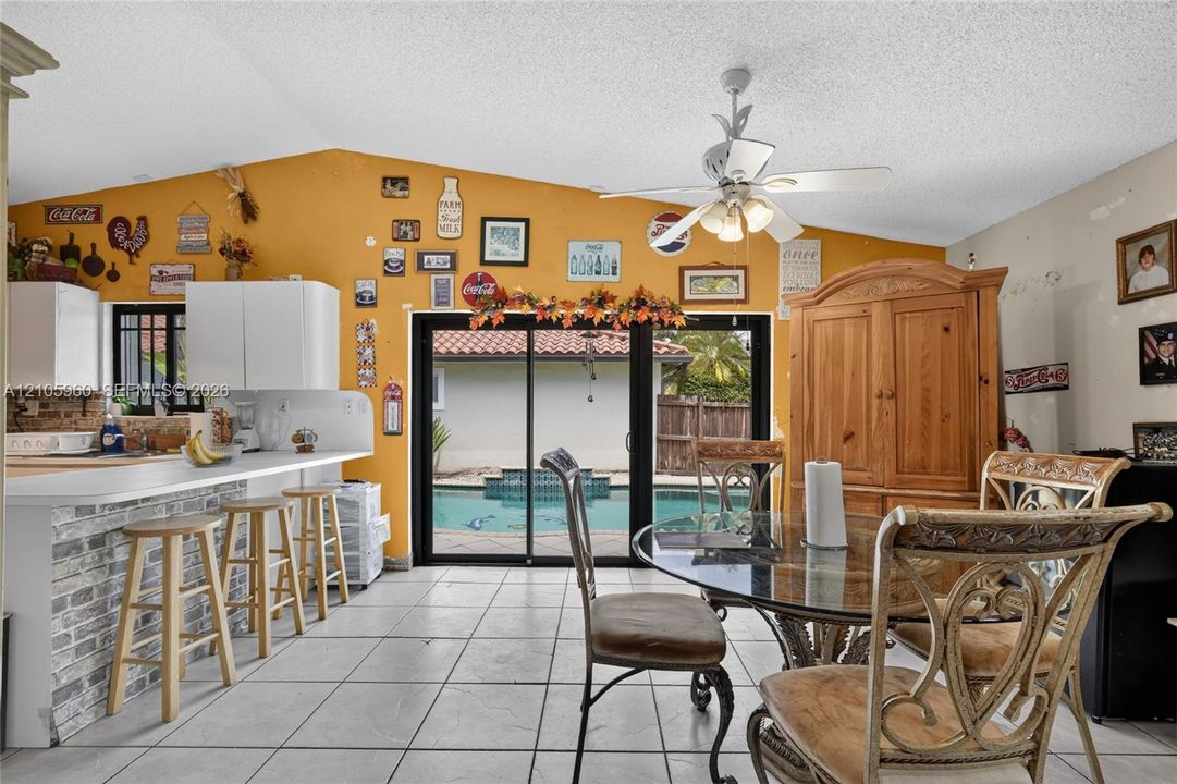 Open-concept room featuring a breakfast bar with stone-finish cladding, neutral tile flooring, a vaulted ceiling with a white ceiling fan, and sliding glass doors