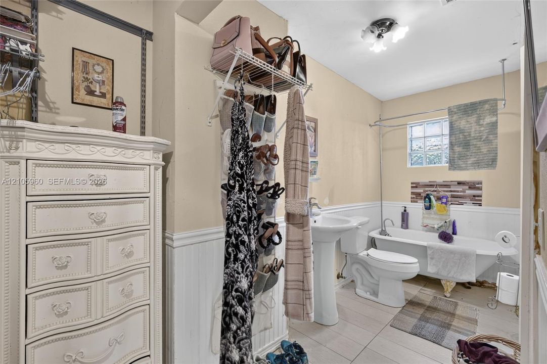 Clawfoot soaking tub, white pedestal sink, tile flooring, beadboard wainscoting, and glass block window