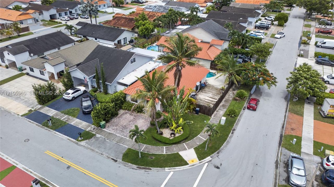 Corner lot residence featuring a barrel tile roof, expansive palm-lined landscaping, and an enclosed backyard with a private swimming pool