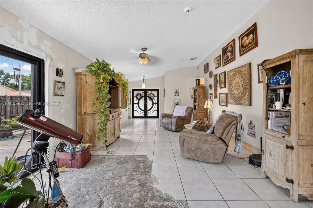 Open-concept living space featuring neutral ceramic tile flooring, dual-entry glass front doors, and a vaulted ceiling with integrated light fixtures