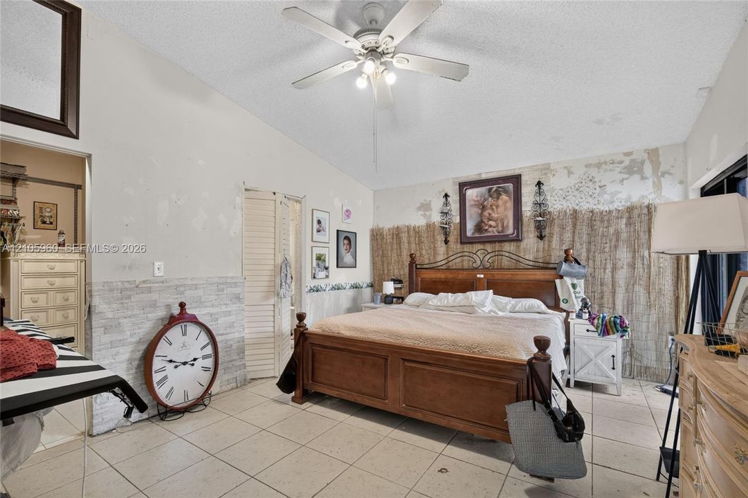 Vaulted ceilings with a central ceiling fan and light fixture, tile flooring, and louvered closet doors