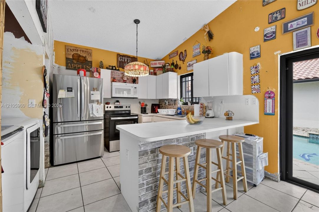 Kitchen featuring stainless steel appliances, a breakfast bar with faux-brick detailing, white cabinetry, ceramic tile flooring, and a vaulted ceiling