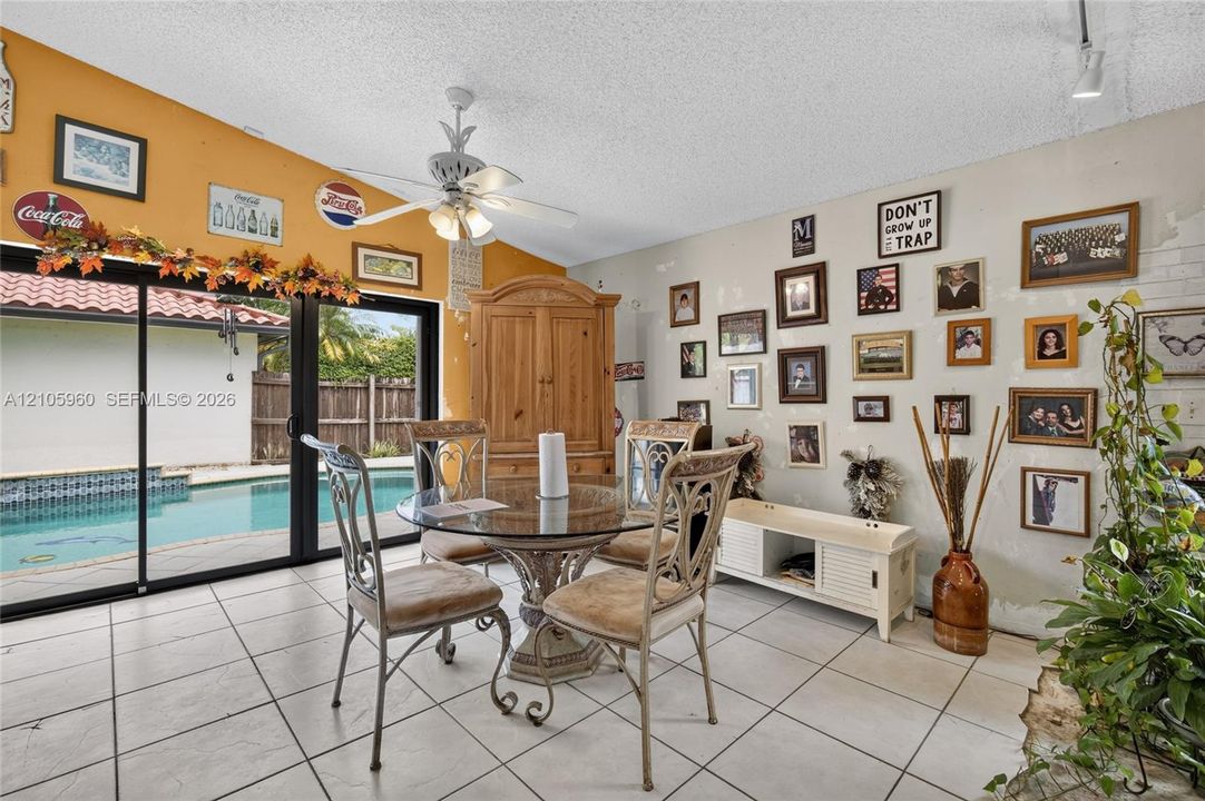 Spacious area featuring ceramic tile flooring, sliding glass doors, white ceiling fan with integrated lighting, and white brick-textured wall accent