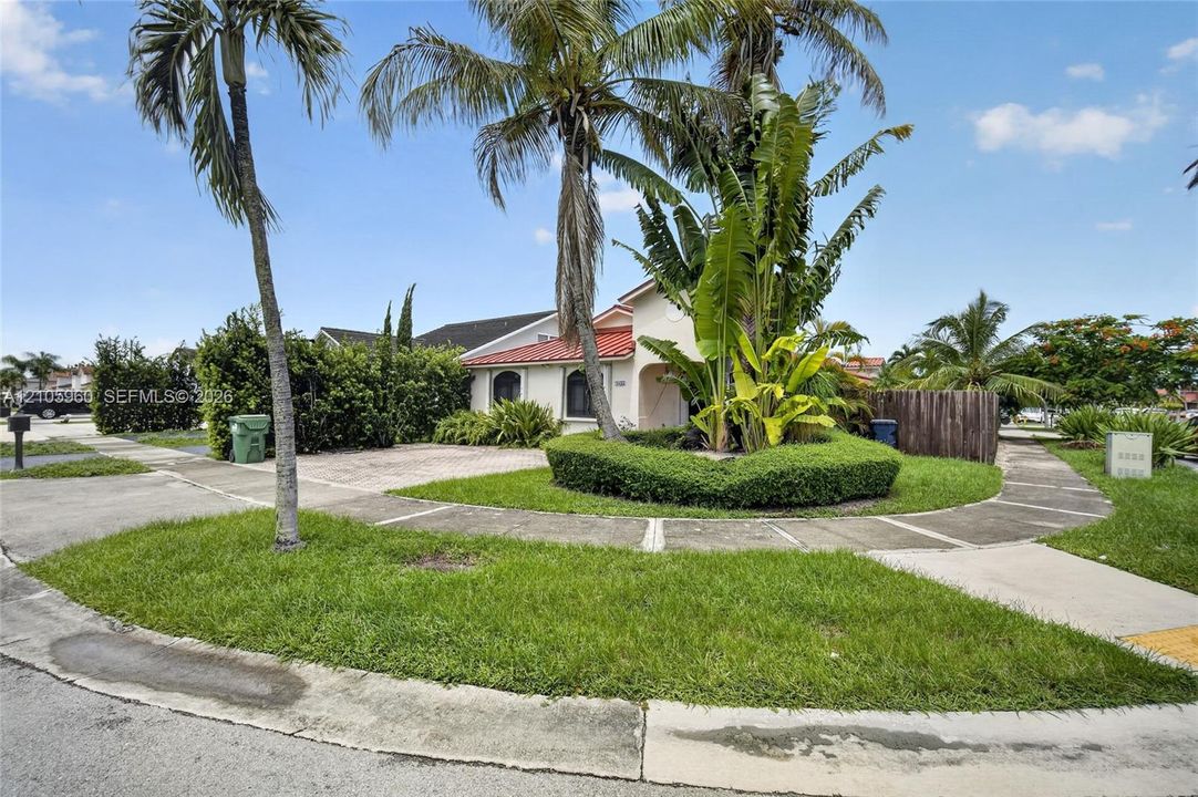 Exterior facade featuring a tile roof, paver driveway, manicured hedges, and mature palm trees