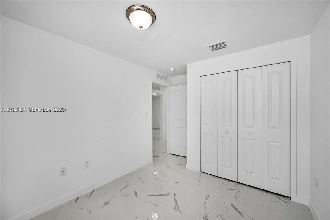 Room featuring polished large-format tile flooring with marbling detail, four-panel bifold closet doors, and a central dome-style ceiling fixture