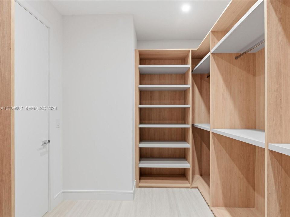 Walk-in closet featuring custom light wood-finish built-in shelving, integrated hanging rods, and wood-finish flooring