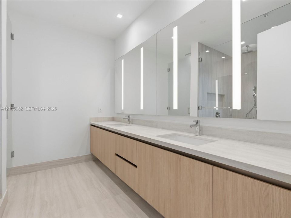Floating wood-finish vanity with dual integrated rectangular sinks, stone-finish countertop, full-width mirrors with vertical integrated LED lighting, and polished chrome faucet fixtures