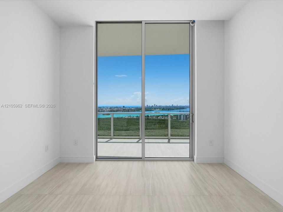 Floor-to-ceiling sliding glass doors, neutral wood-finish flooring, and an attached balcony with metal railing