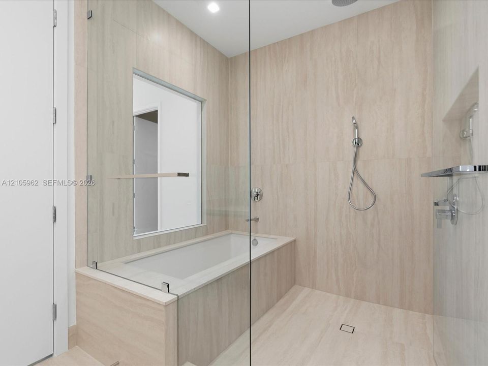 Walk-in shower and tub combination featuring floor-to-ceiling stone-finish tiling, a frameless glass enclosure, polished chrome fixtures, and a hand-held shower wand
