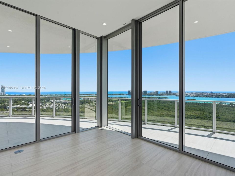 Floor-to-ceiling glass walls with metal framing, expansive private balcony, neutral tile flooring, and recessed ceiling lighting