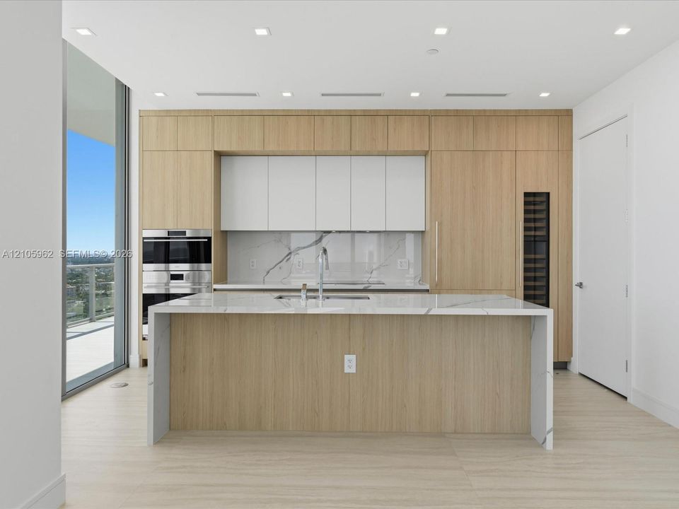 Kitchen featuring a stone waterfall-edge island, wood-finish cabinetry, built-in stainless steel double wall ovens, integrated wine storage, and floor-to-ceiling glass windows