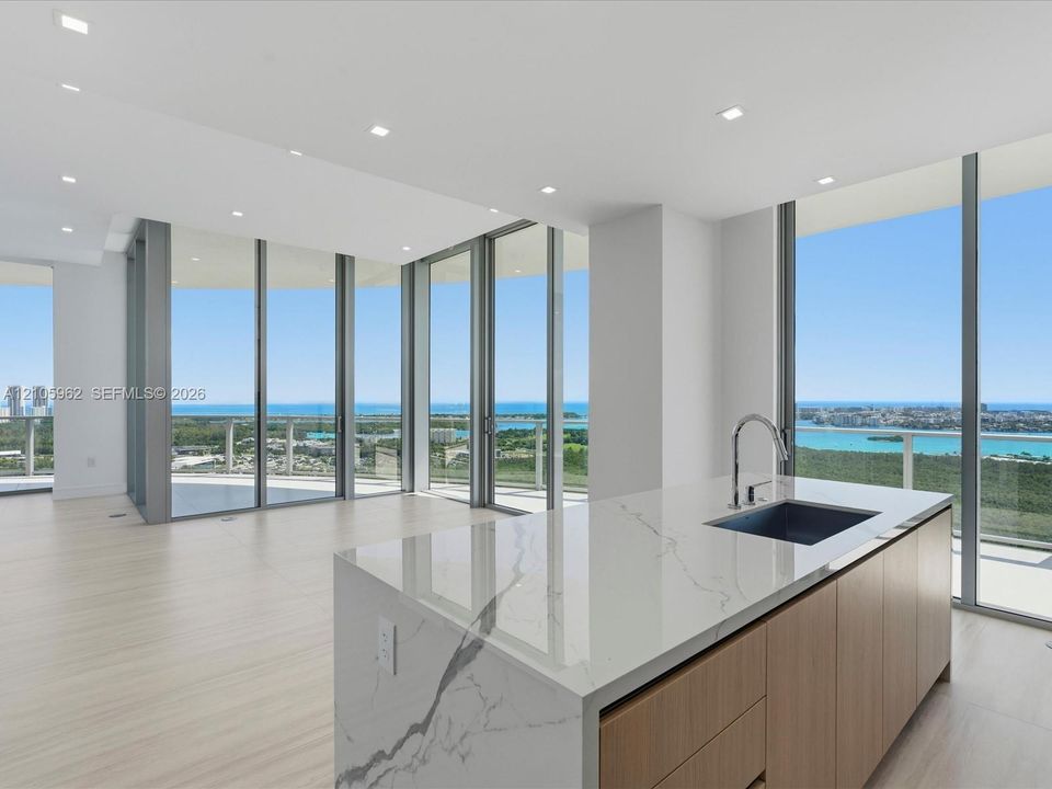 Kitchen island featuring a waterfall-edge stone countertop, undermount sink, and wood-finish cabinetry
