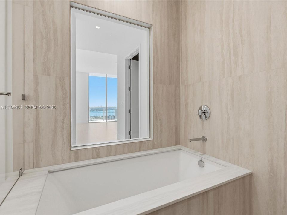 Built-in deep soaking tub featuring stone-finish wall cladding, polished chrome wall-mounted fixtures, and a glass-paneled opening