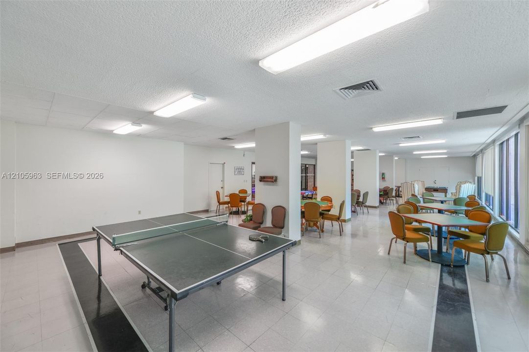 Large open-concept interior featuring light-colored tile flooring with decorative dark accents, structural support pillars, and linear ceiling-mounted lighting