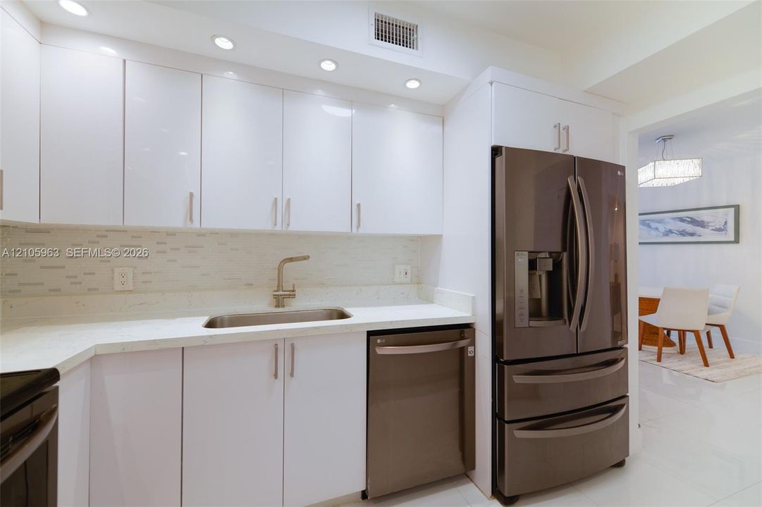Kitchen featuring high-gloss white cabinetry, light-toned stone-surface countertops, a mosaic tile backsplash, stainless steel appliances, and recessed lighting