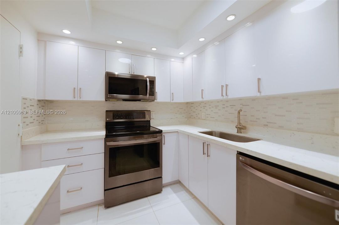Kitchen featuring white high-gloss cabinetry, stainless steel appliances, white solid-surface countertops, mosaic tile backsplash, and recessed lighting