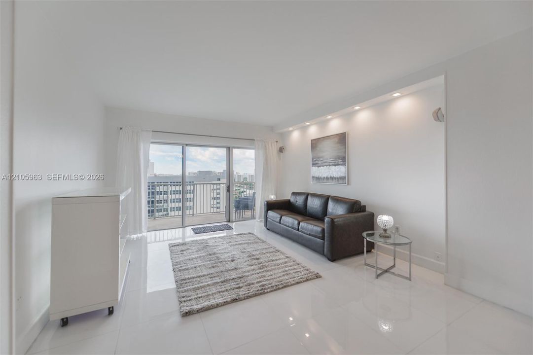 Living area featuring polished tile flooring, recessed ceiling lighting, and a large sliding glass door opening to a balcony