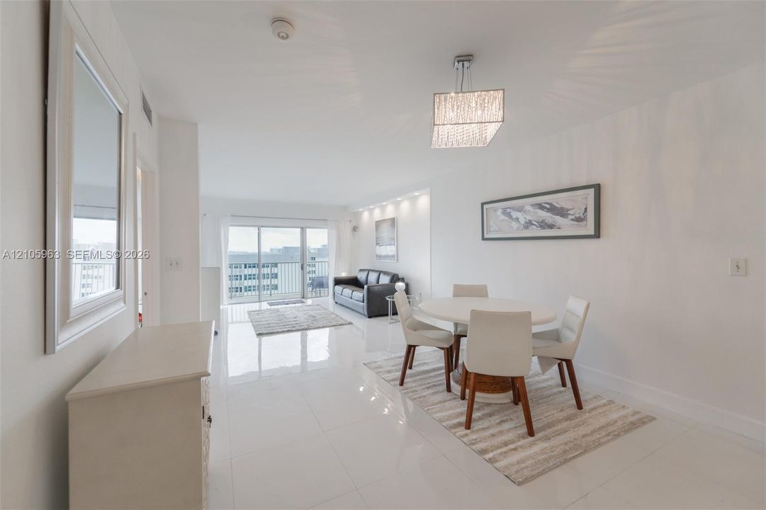 Open-concept living space featuring high-gloss tile flooring, recessed ceiling lighting, a tiered crystal-style chandelier, and sliding glass balcony doors