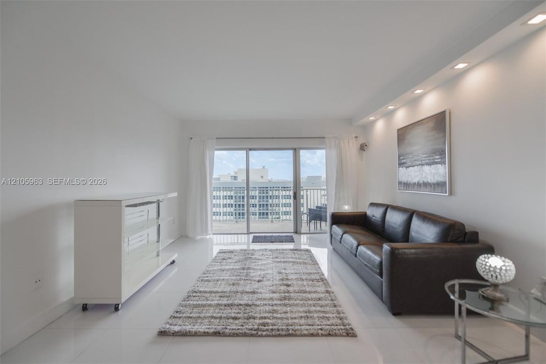 Open-concept living space featuring high-gloss tile flooring, recessed cove lighting, and floor-to-ceiling sliding glass doors providing access to an outdoor balcony