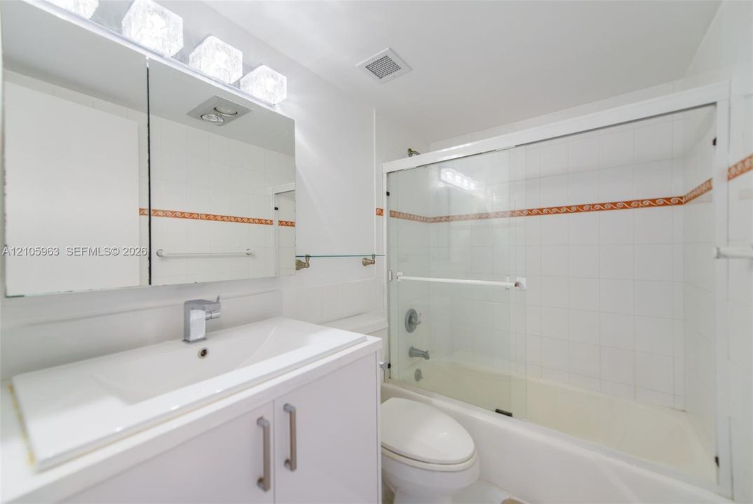 Bathroom featuring a vanity with an integrated sink, tri-light fixture, medicine cabinet, and a tub-shower combination enclosed by glass sliding doors