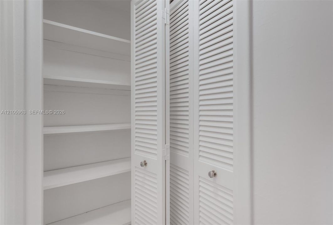 Storage closet featuring white louvered bifold doors, chrome round knobs, and interior shelving