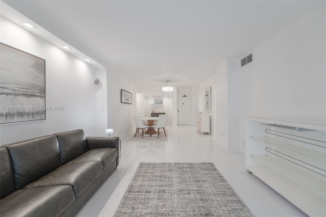 Open-concept interior featuring smooth-finish tile flooring, recessed ceiling lighting, and a built-in glass shelving unit
