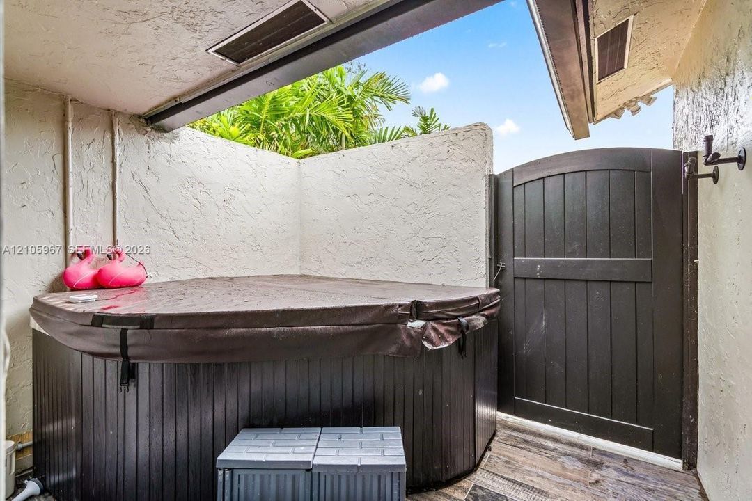 Covered outdoor spa area featuring a wood-panel base, privacy walls with stucco finish, and an arched wooden gate