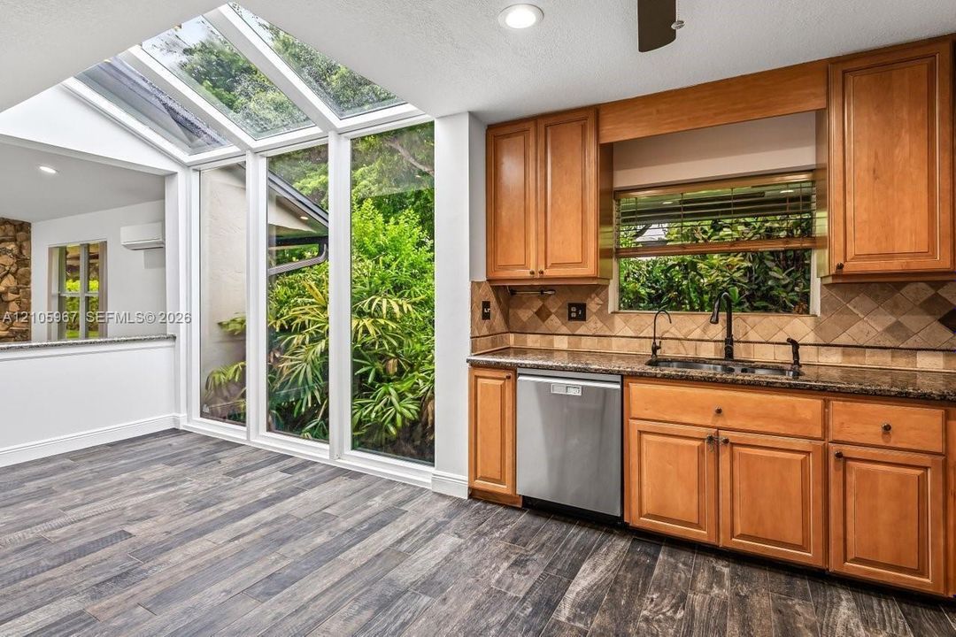 Kitchen featuring floor-to-ceiling windows with integrated skylights, wood-finish cabinetry, stone-surface countertops, stone tile backsplash, and wood-finish flooring