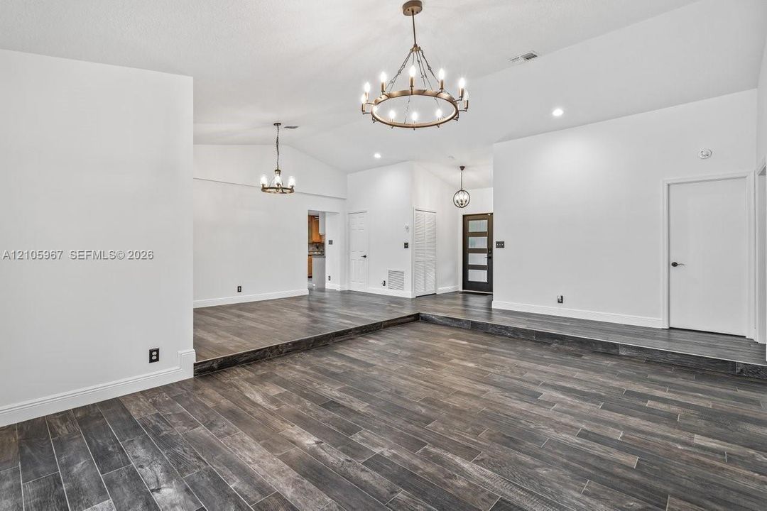 Vaulted ceilings, wood-finish tile flooring, recessed lighting, and multi-arm chandelier fixtures