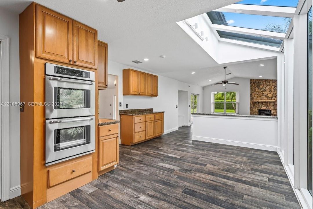 Kitchen featuring wood-finish cabinetry, stainless steel double wall ovens, wood-finish flooring, extensive skylights, and a stone-accented fireplace