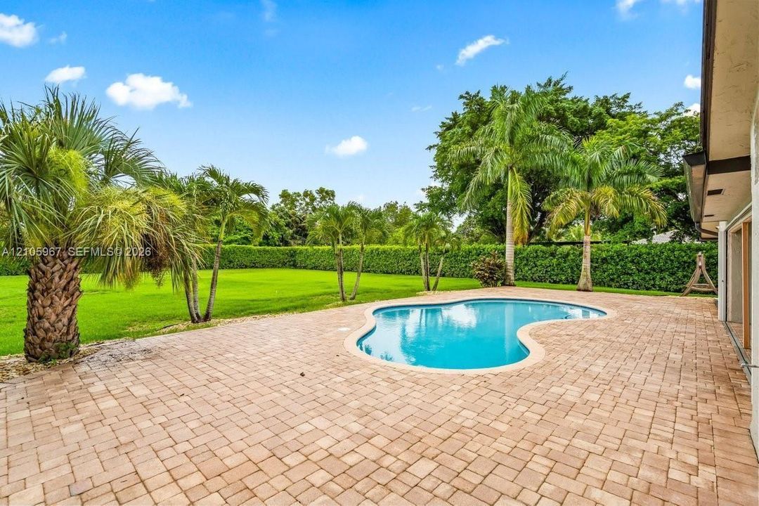 Backyard featuring a free-form pool, expansive brick paver patio, manicured lawn, and mature perimeter landscaping