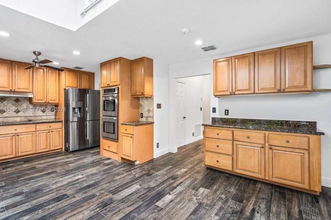 Kitchen featuring light-tone wood cabinetry, dark stone countertops, stainless steel double wall ovens, a stainless steel refrigerator, and wood-finish flooring