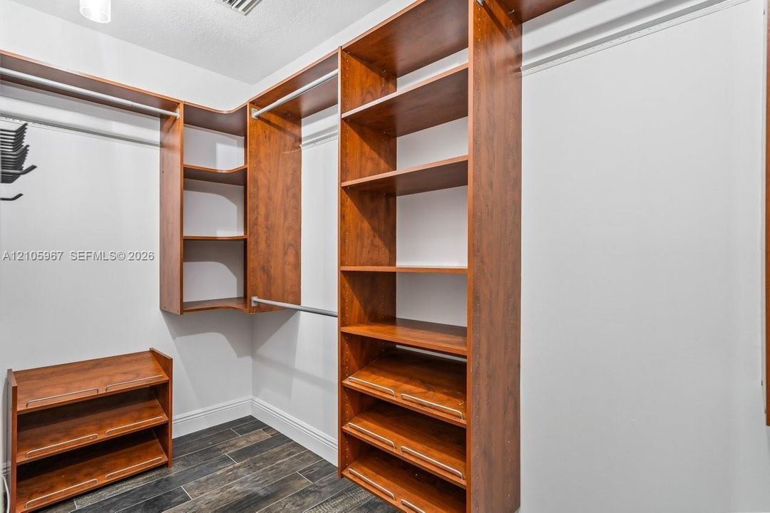 Walk-in storage area featuring custom wood-finish shelving, integrated hanging rods, tiered shoe storage, and wood-finish flooring