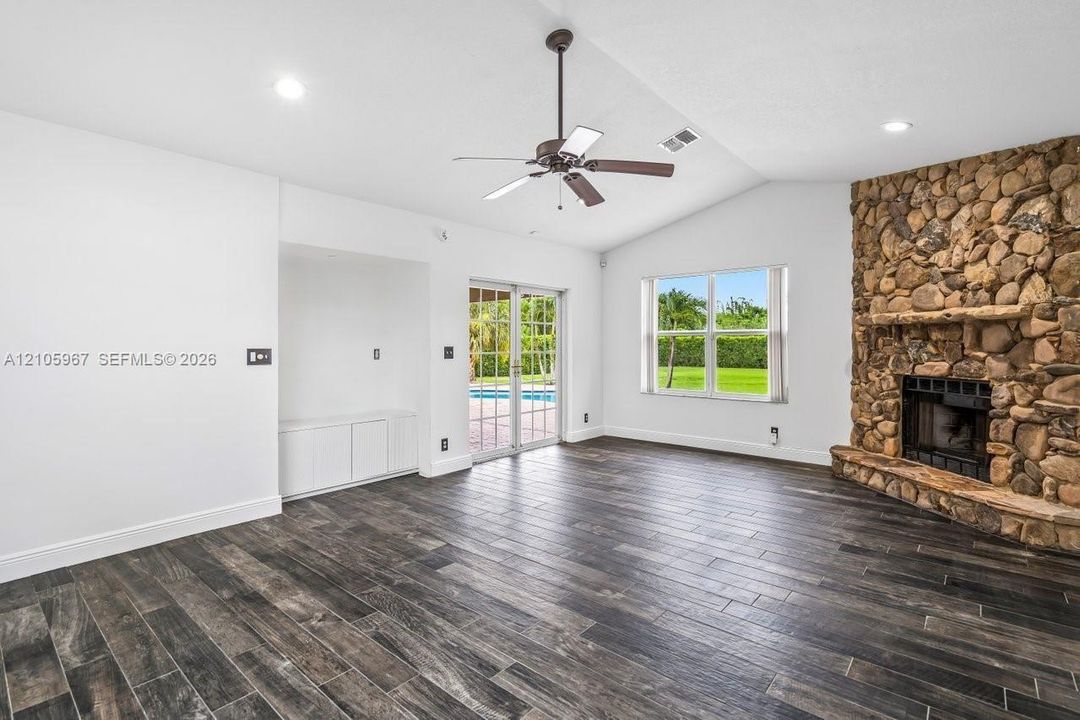 Vaulted ceilings, wood-finish flooring, floor-to-ceiling natural stone fireplace, built-in cabinetry, and sliding glass doors