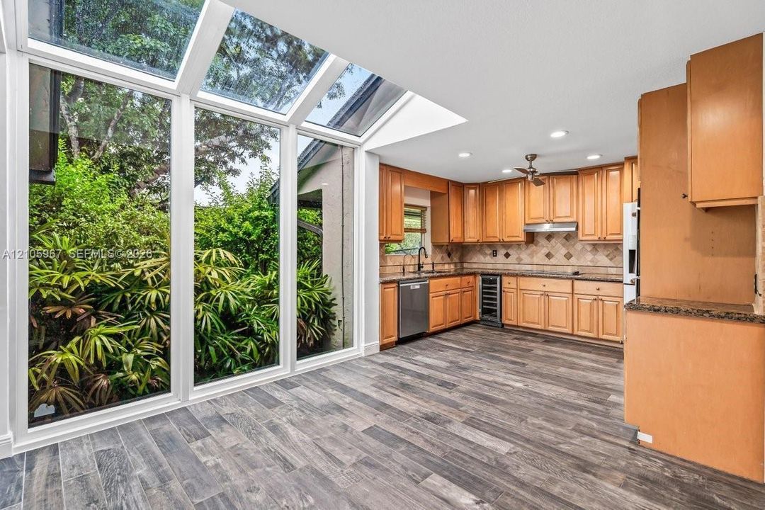 Kitchen featuring full-height glass walls and sloped skylights, wood-finish flooring, shaker-style cabinetry, and integrated wine refrigeration
