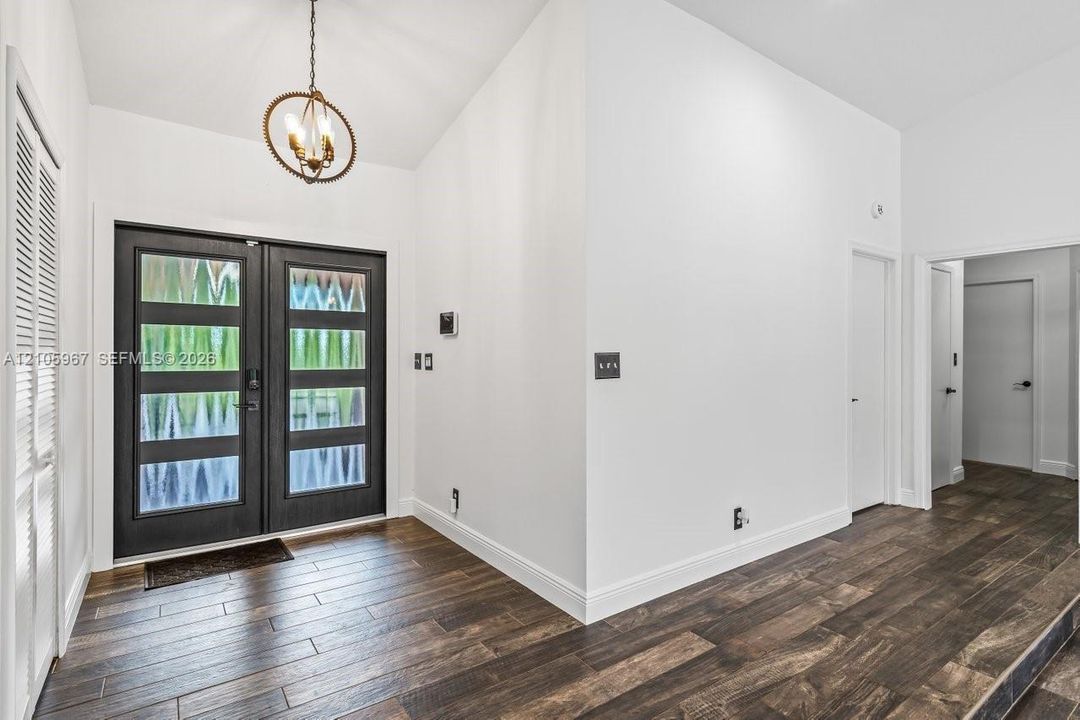 Double-door entry with glass panels, wood-finish flooring, and a circular orb-style chandelier